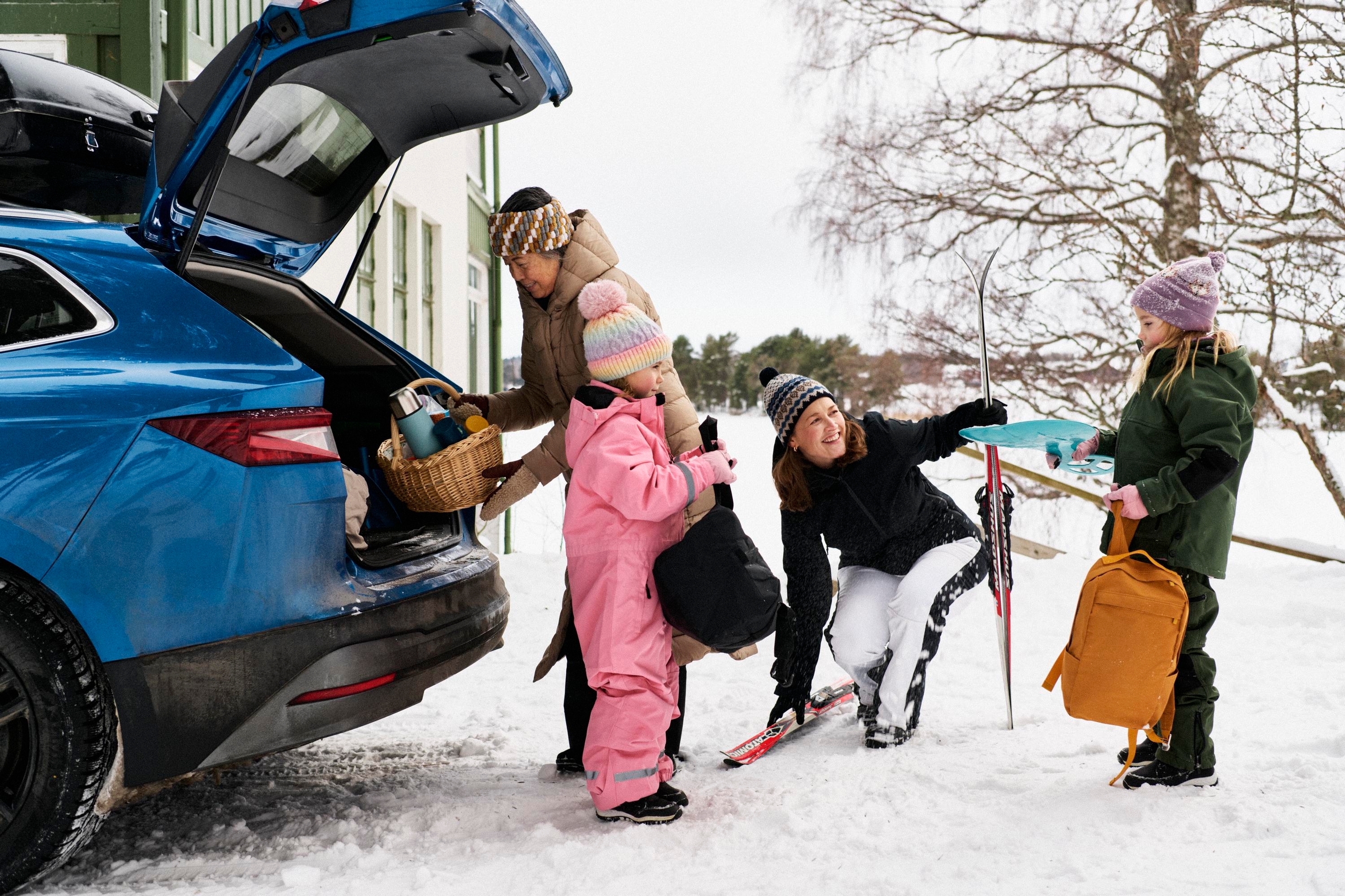 Vuxna och barn packar en bil med picknickkorg och skidor