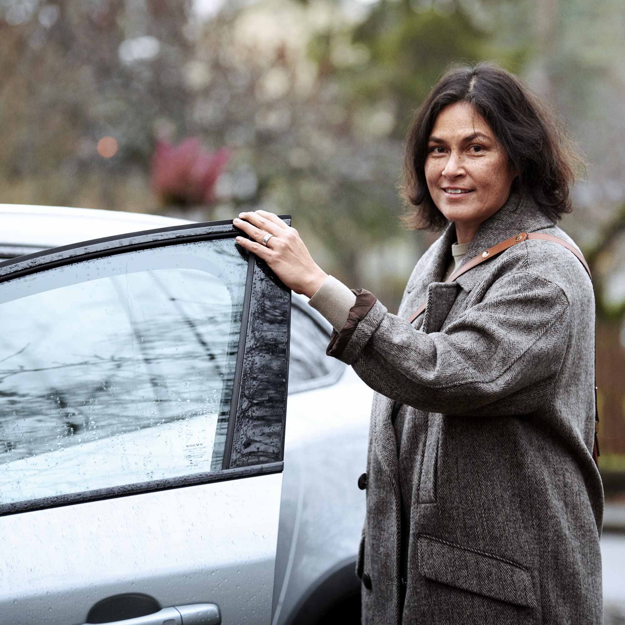 Kvinna med grå kappa håller på att kliva in i en bil en höstdag