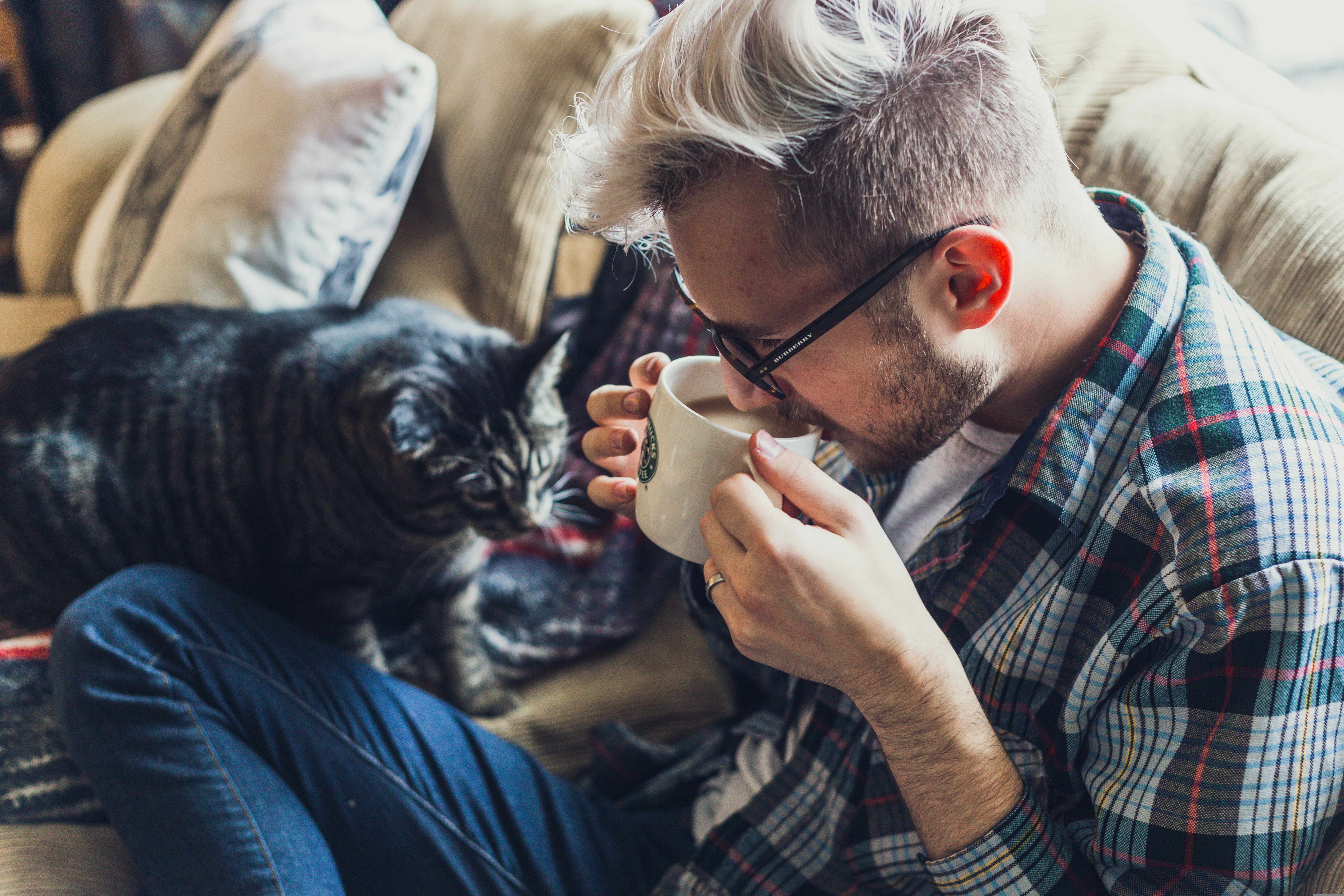 Ung man relaxar med kaffe och en katt 
